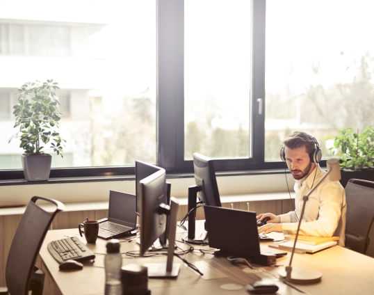 Afbeelding genomen in een kantoor met een man erop die kijkt op zijn scherm en een headset op heeft